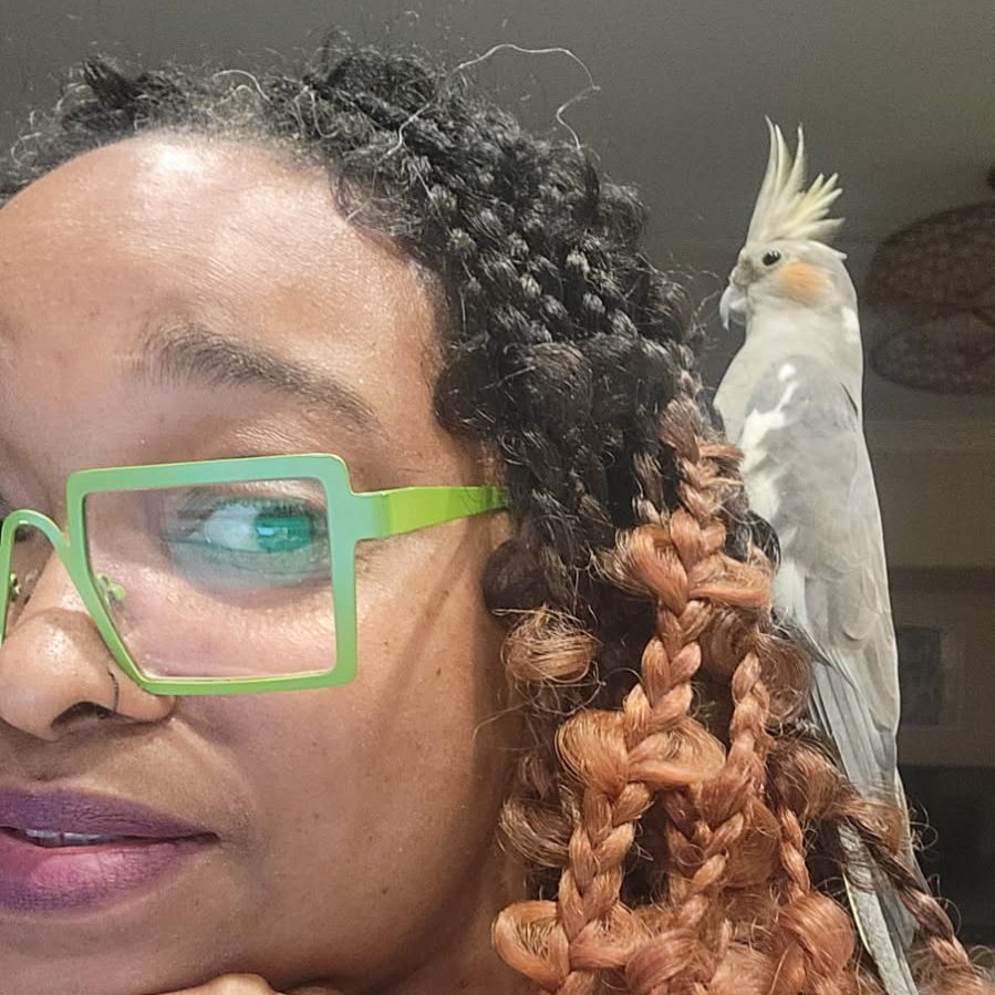 A woman with glasses smiles while holding a dog outdoors.